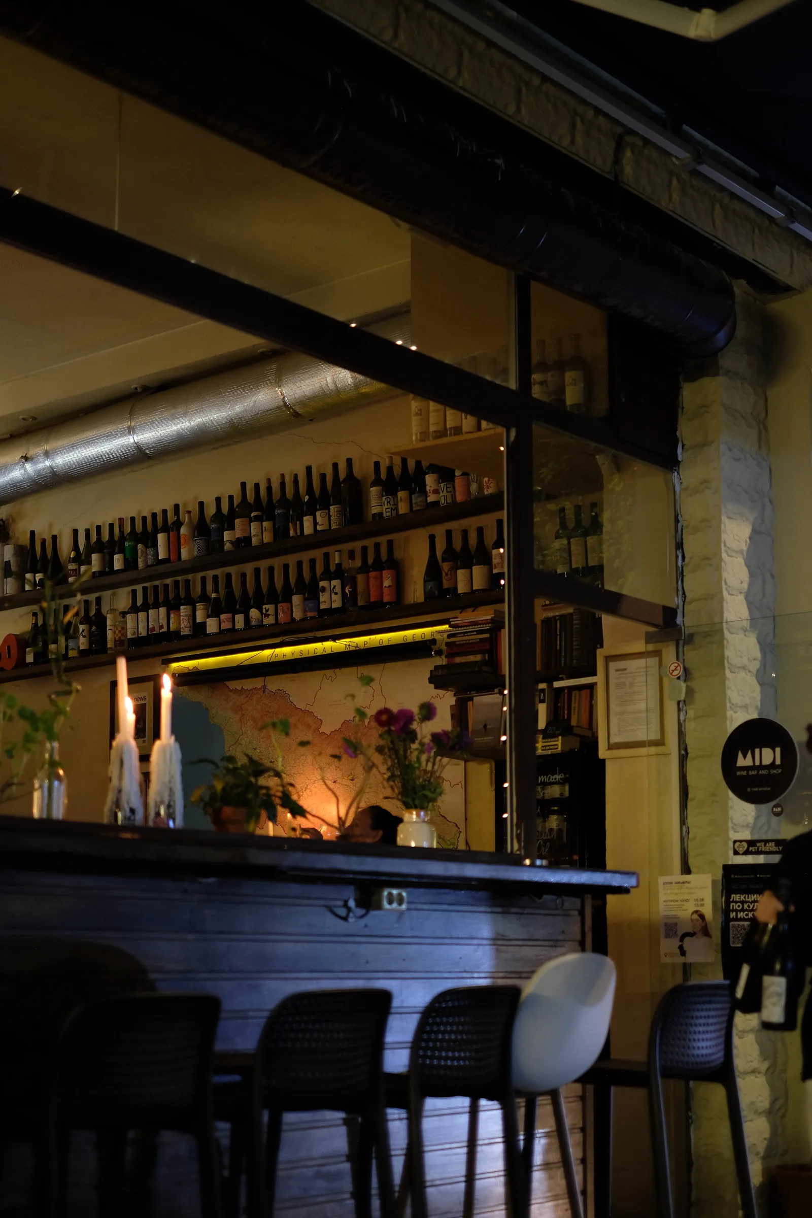 The candlelit interior of MIDI Wine Bar & Shop seen from the pavement at night.