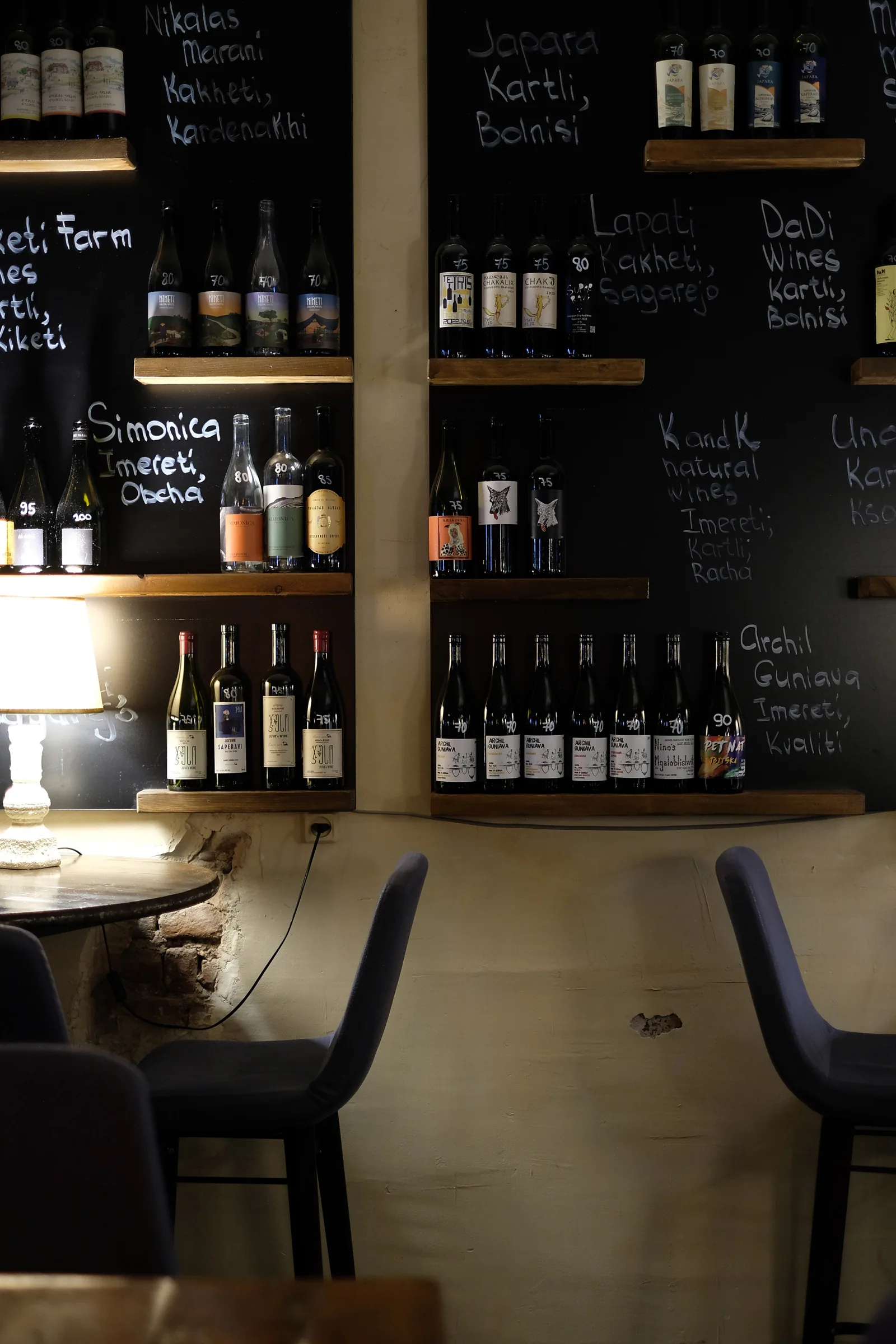 Bottles arranged on shelves against chalkboard walls marked with Georgian wine regions and producers.