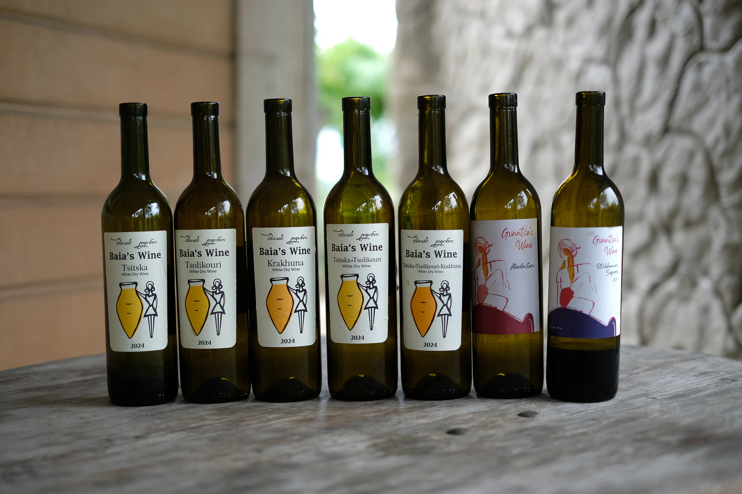 Seven bottles of Baia's Wine and Gvantsa's Wine lined up on a wooden table.