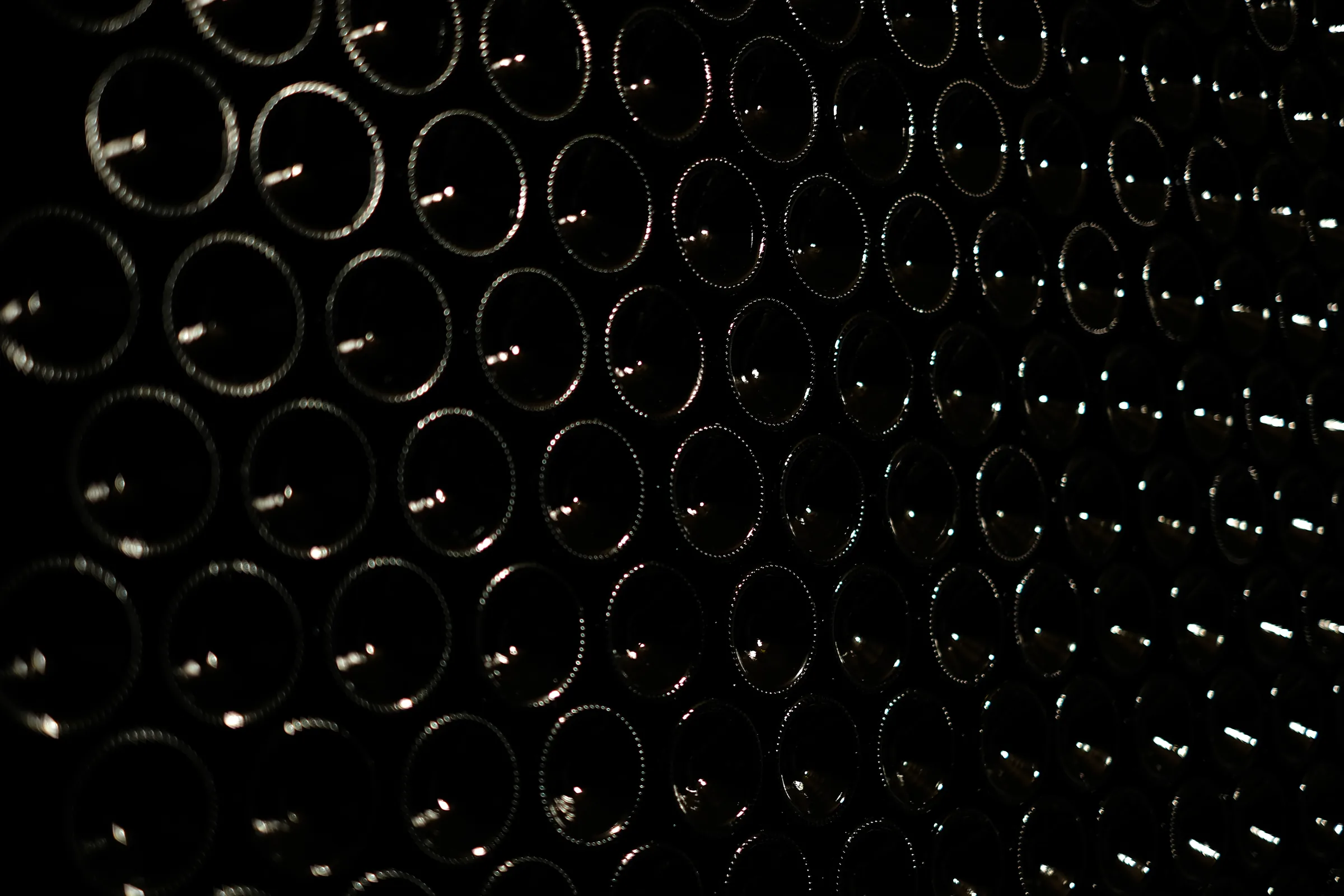 Rows of unlabelled wine bottles stacked horizontally in the dark cellar.